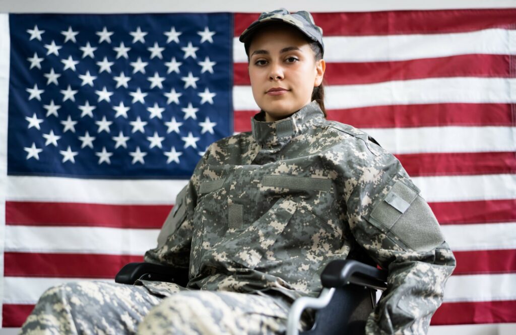 A woman in a wheelchair, wearing a military uniform. The background of the image is the American flag.